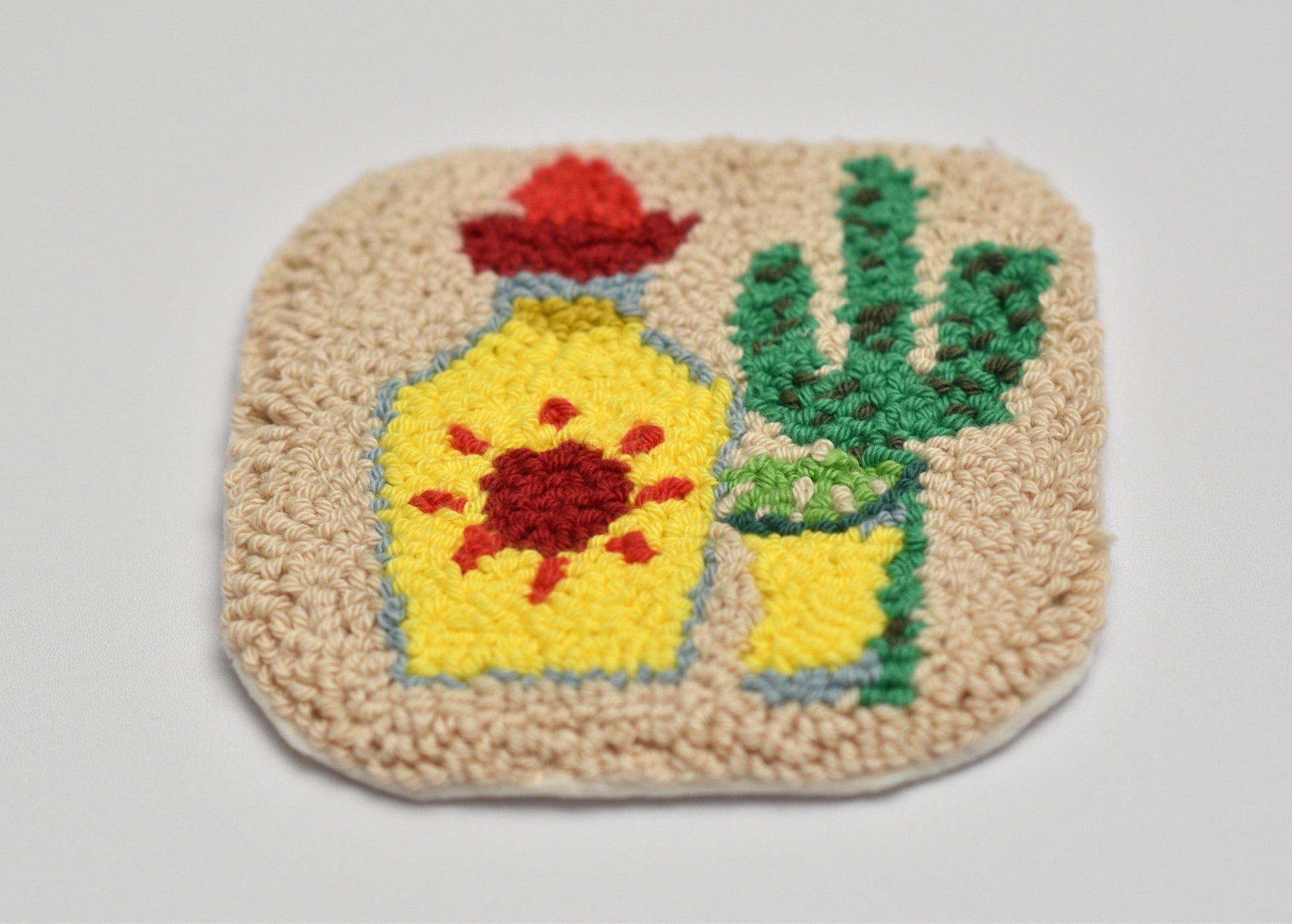 Decorative punch needled coaster with a Tequila bottle and cactus design on a plain background