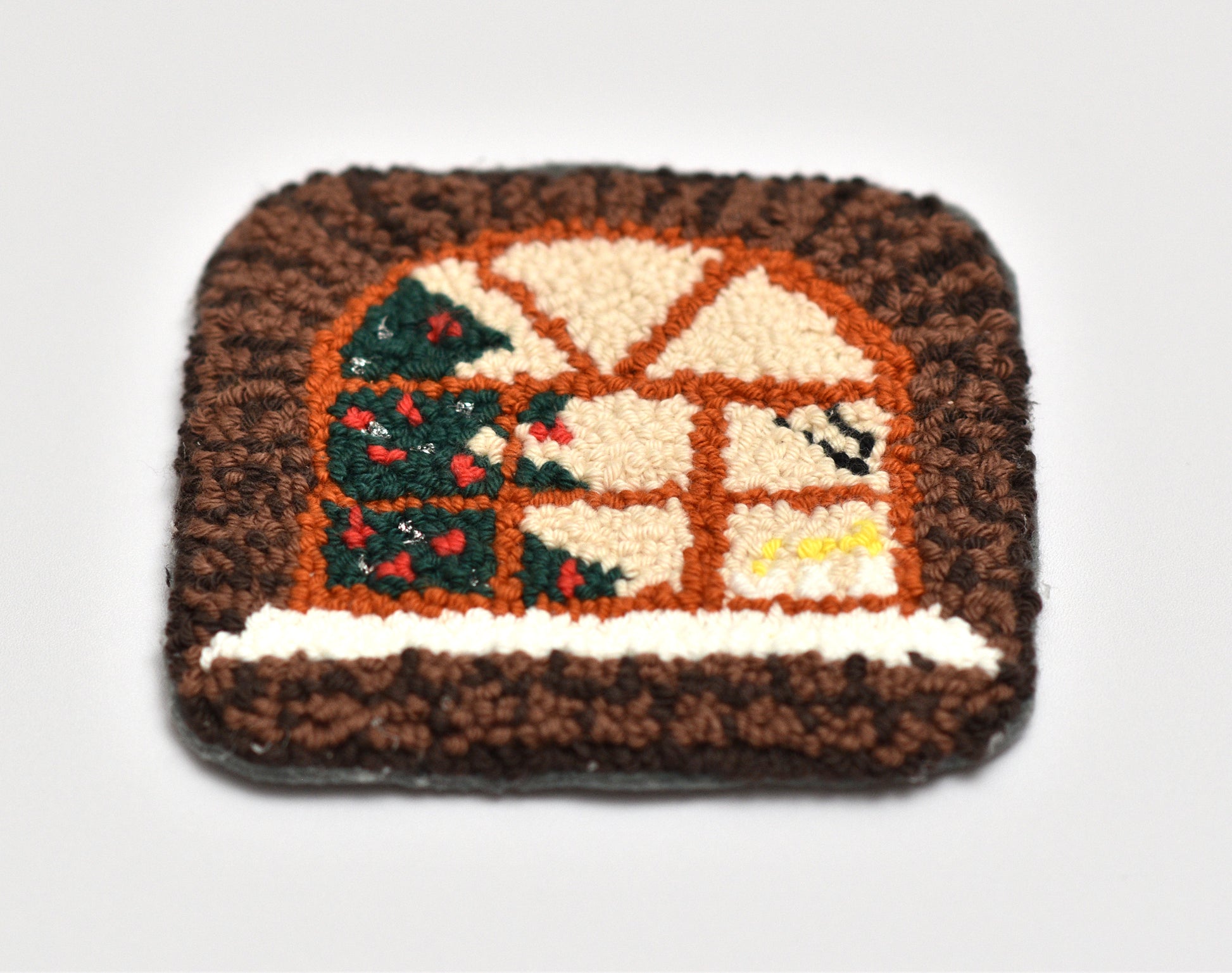 Decorative punch needled mug rug with a house and tree design on a white background
