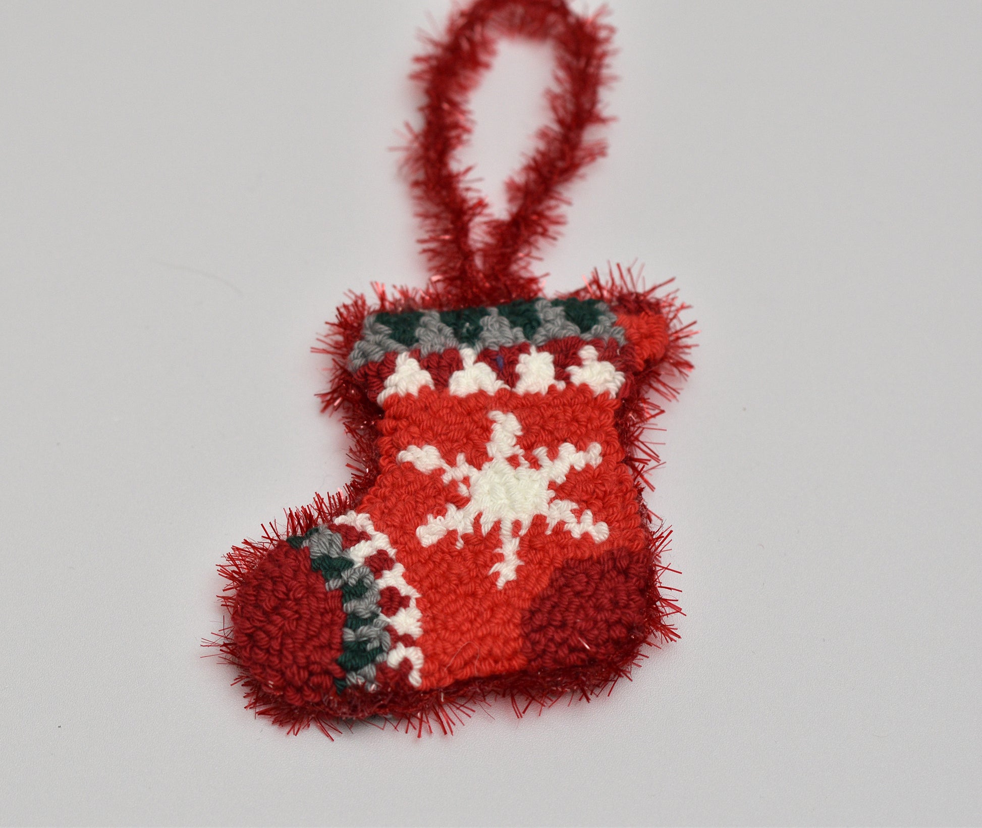Red punch needled Christmas stocking ornament with a white snowflake on a light gray background