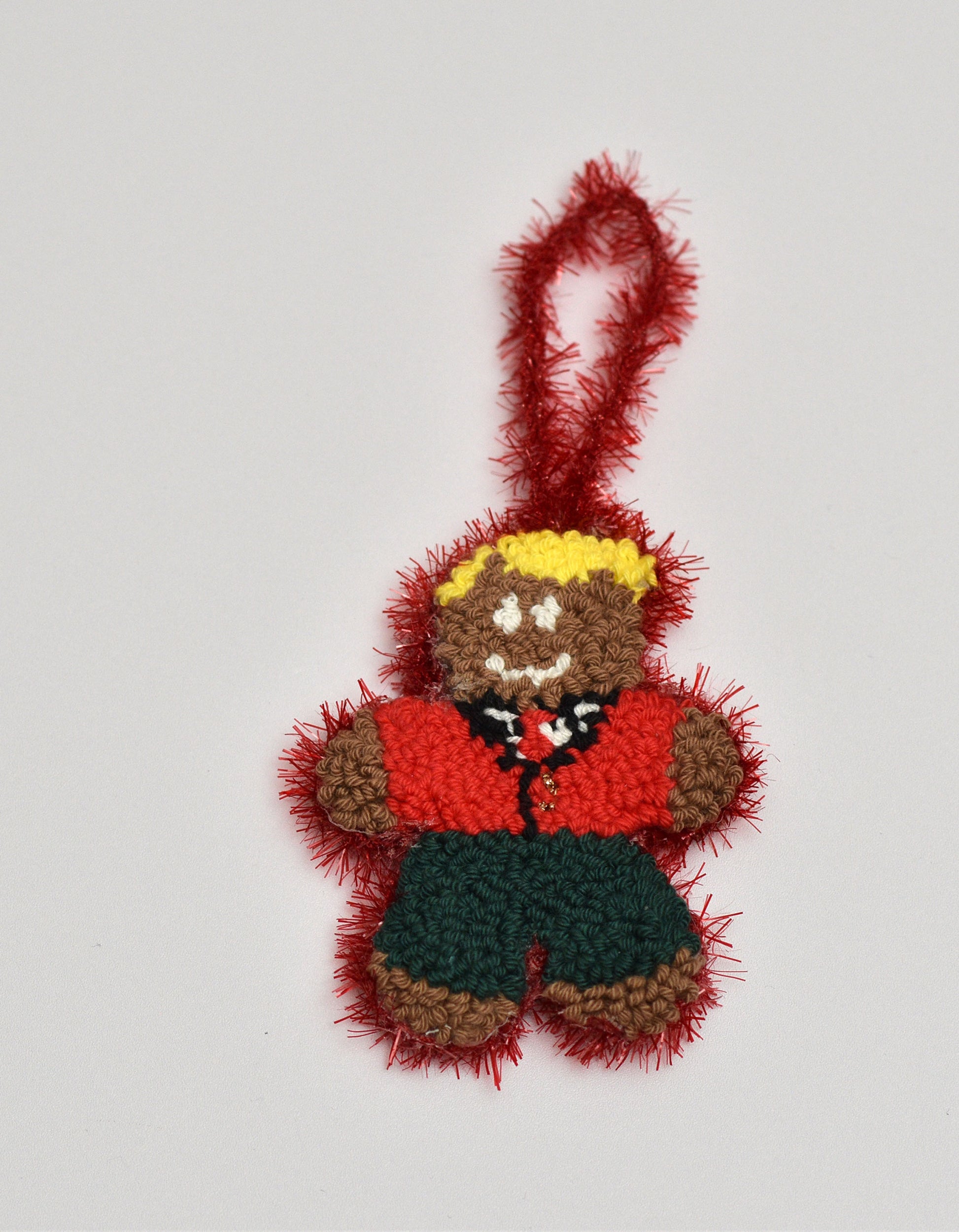 Punch needled gingerbread man ornament with a red jacket on a light gray background