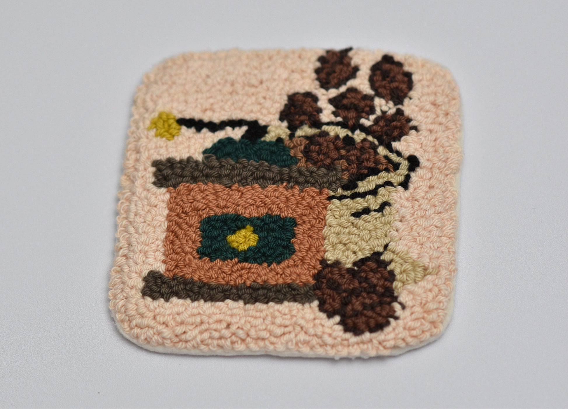 Square punch needled coaster with a coffee grinder and coffee beans design on a plain background