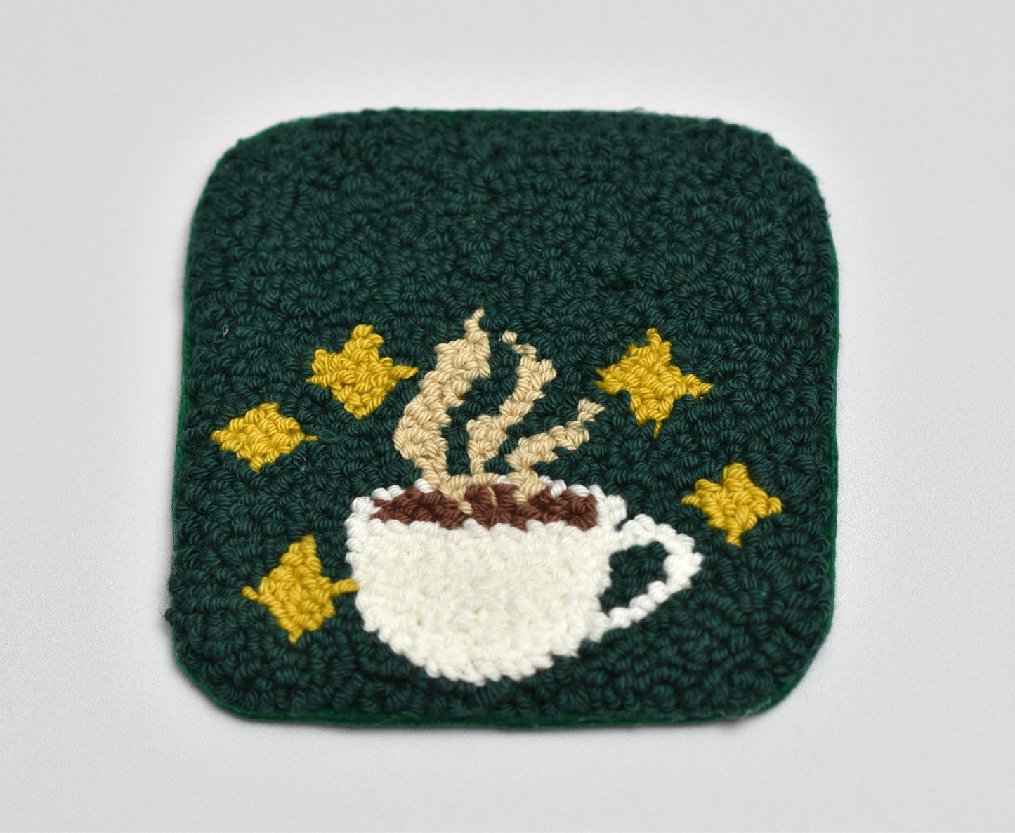 Punch needled coaster with a coffee cup and stars design on a green background