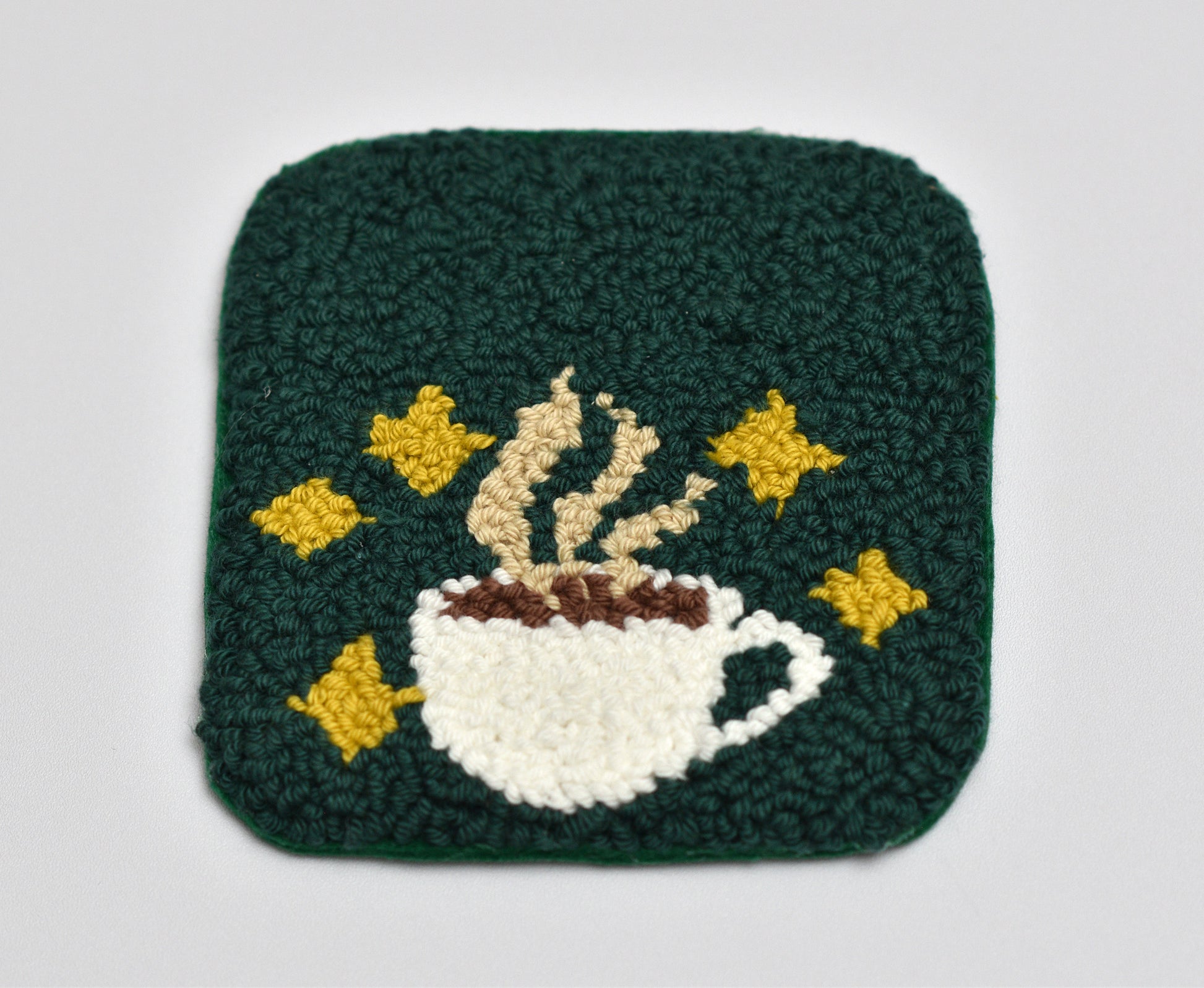 Punch needled coaster with a coffee cup and stars design on a green background