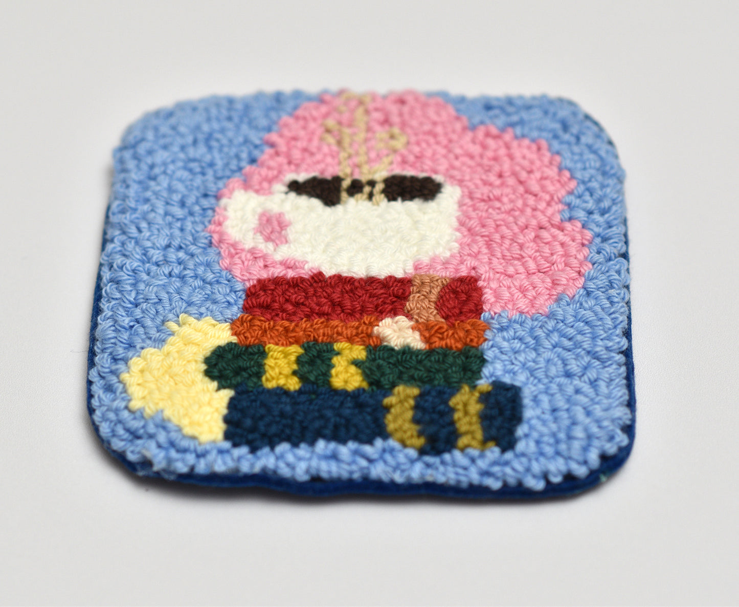 Embroidered coaster with books and coffee cup on a blue background