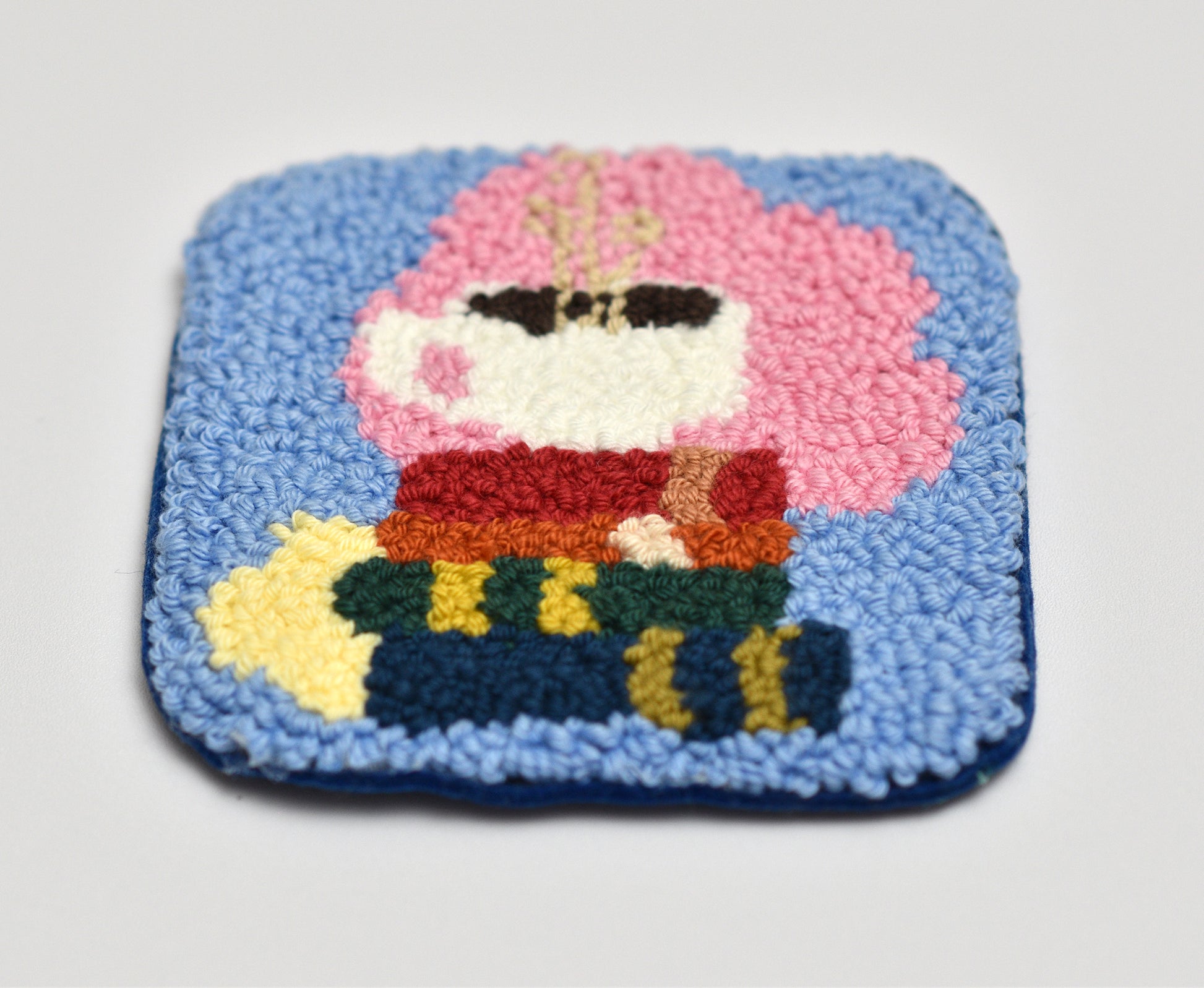 Embroidered coaster with books and coffee cup on a blue background