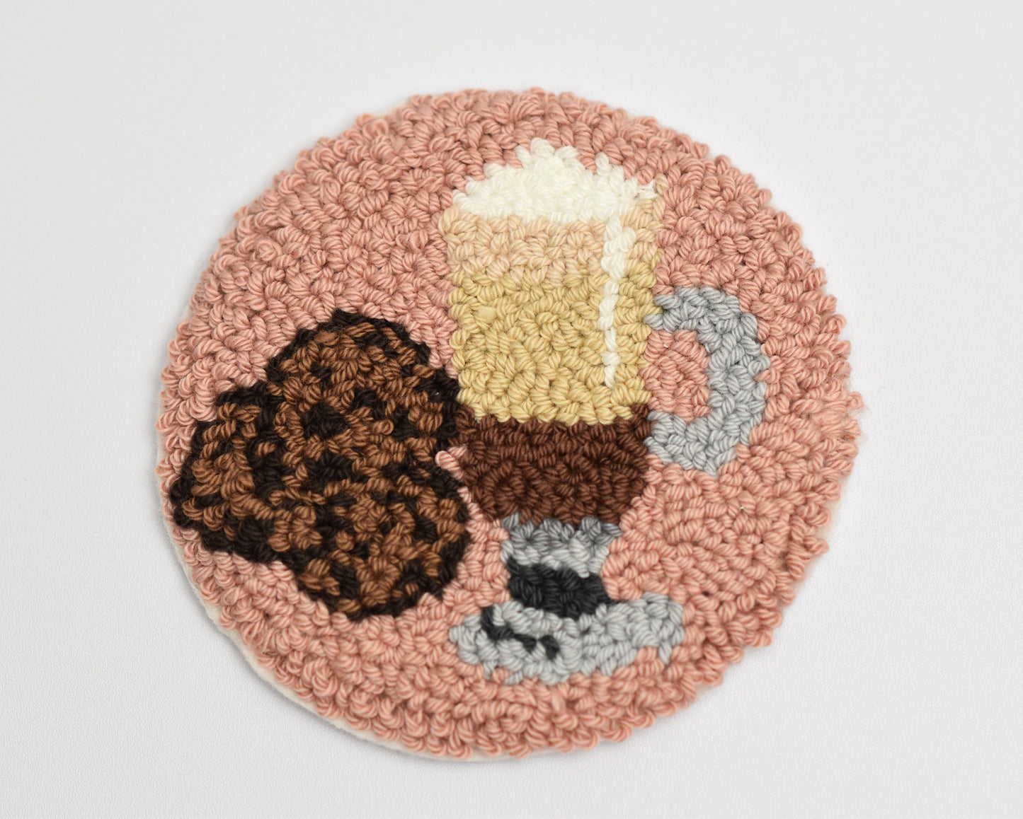 Round punch needle coaster with a coffee Latte cup and cookie design on a light gray background
