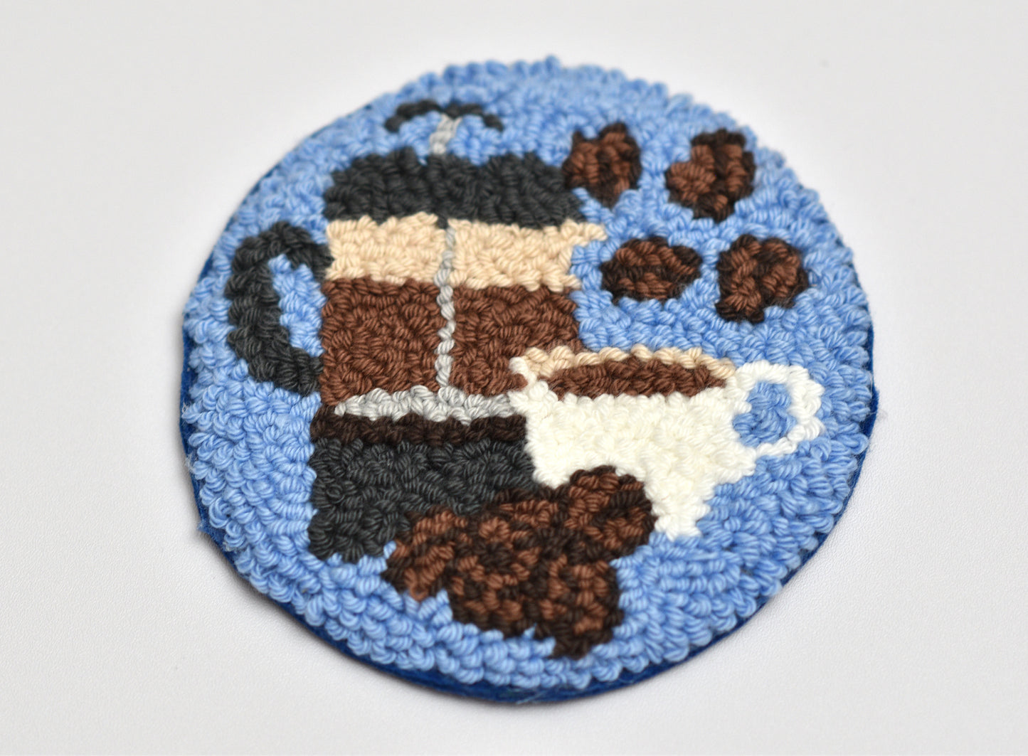 Round blue coaster with coffee-themed design featuring a French press, cup, and coffee beans on a white background.