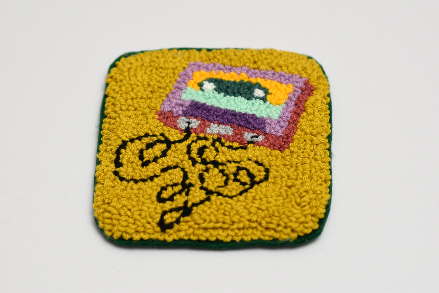 Square punch needle coaster with cassette tape design and text on a yellow background