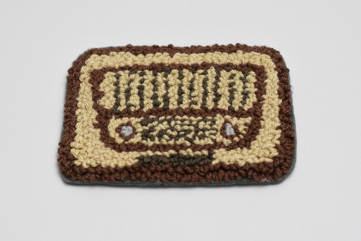 Punch needle coaster with a retro radio design on a plain background