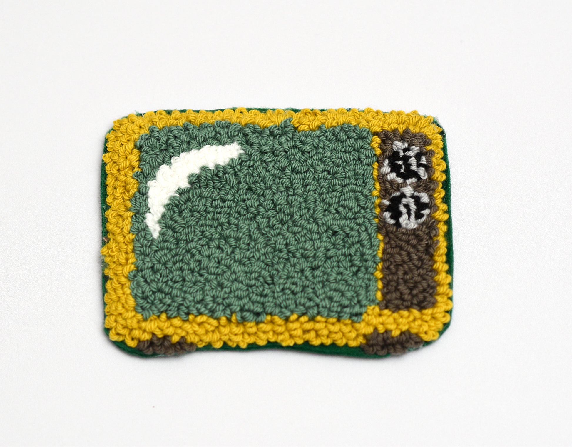 Punch needle coaster with green center, yellow border retro TV designed, and white and brown accents on a white background