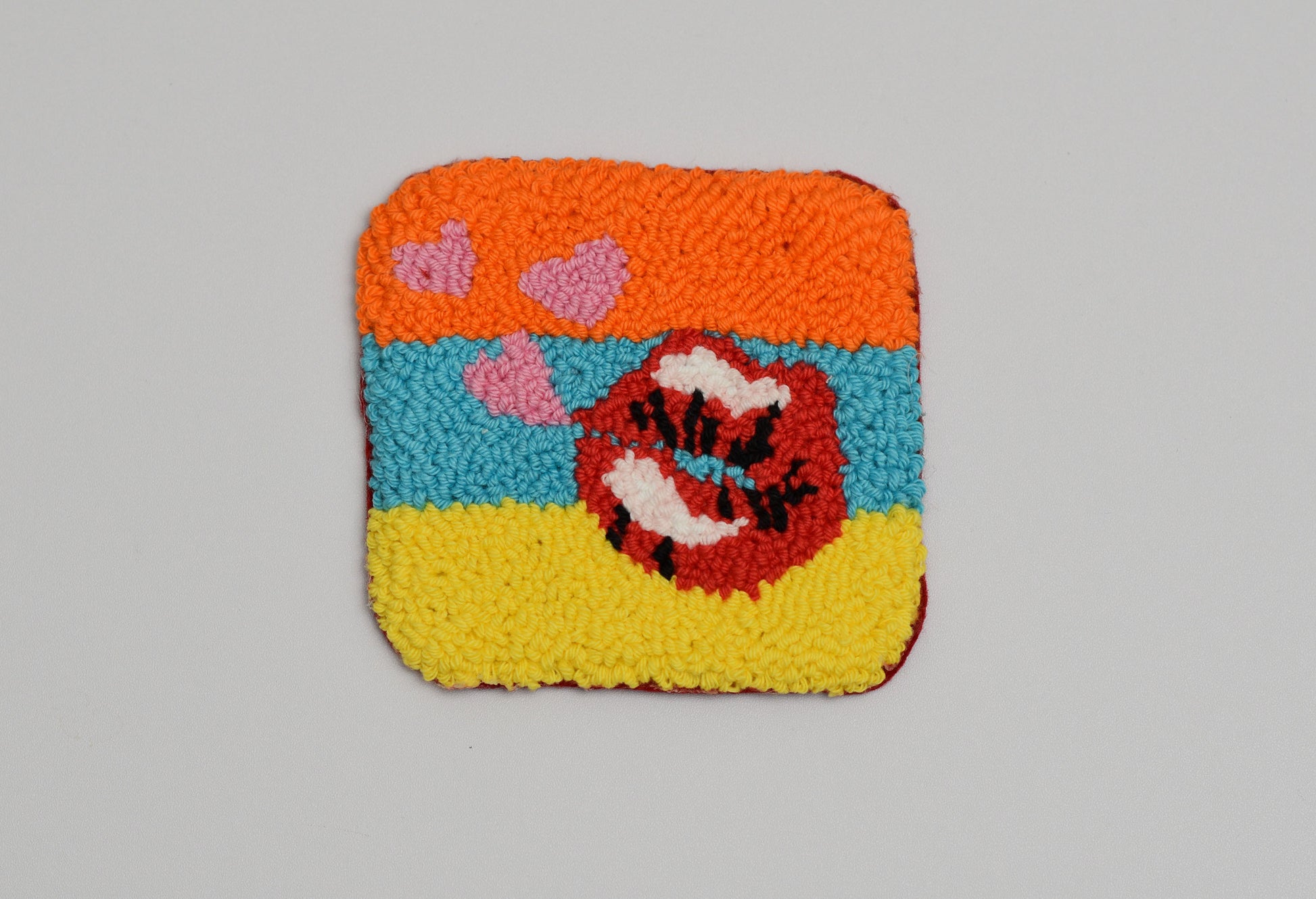 Colorful woven square coaster with a retro kiss design and pink accents on a gray background