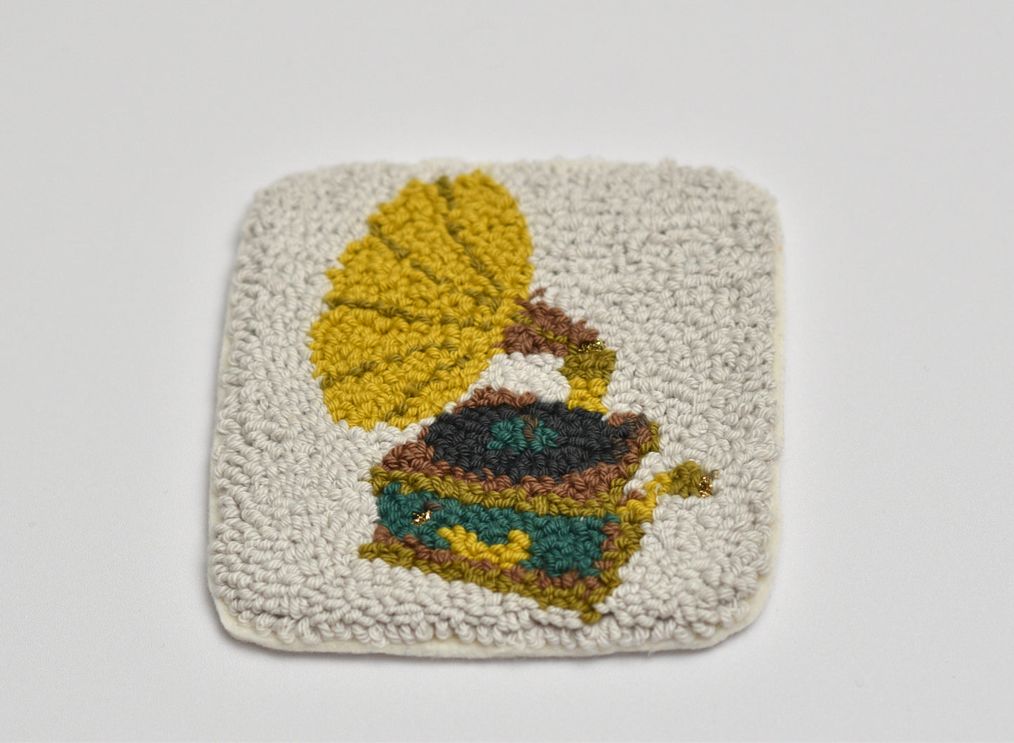 Punch needled square coaster with gramophone designed pattern of yellow, green, and brown on a light gray background