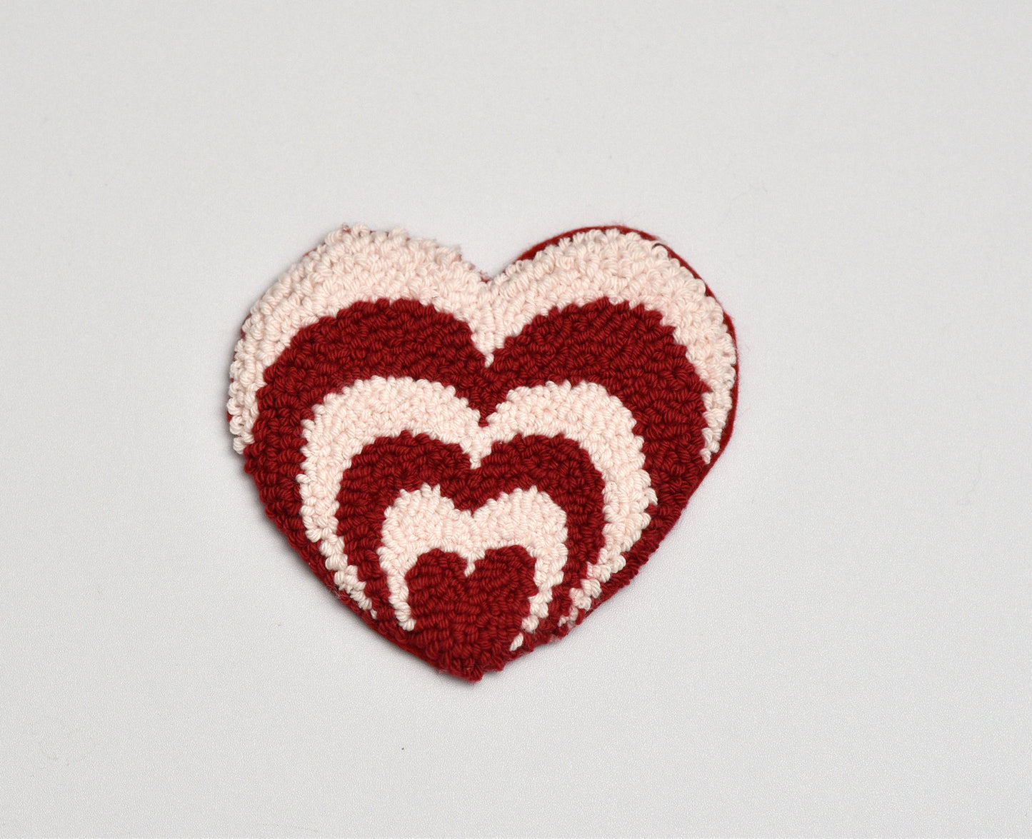 Heart-shaped crochet pattern in red and beige on a light gray background