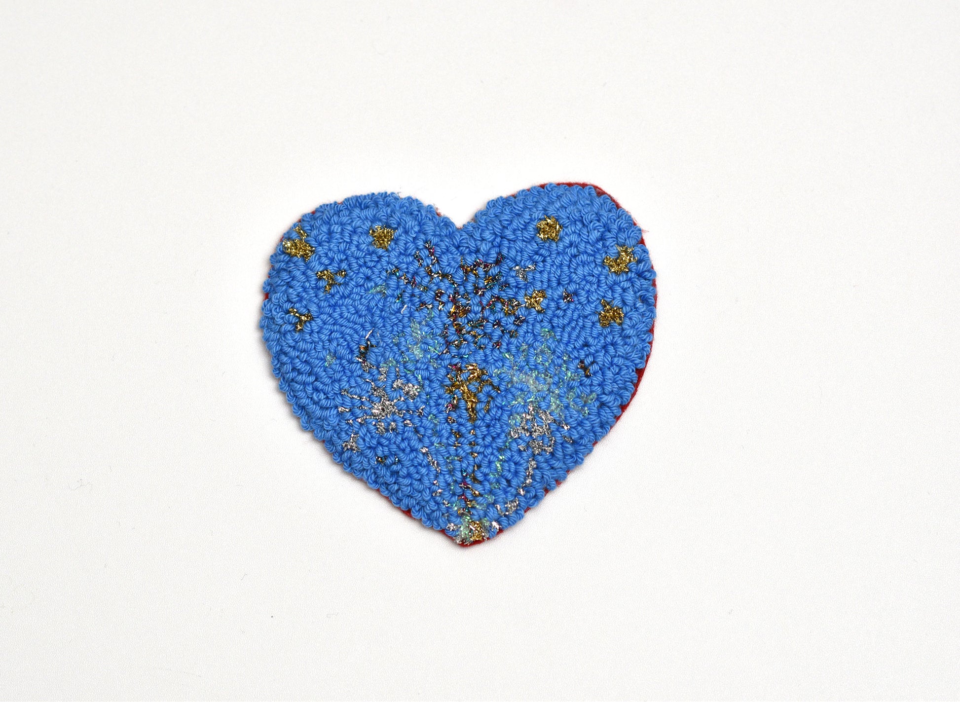 Blue heart-shaped punch needle coaster with gold embellishments on a white background