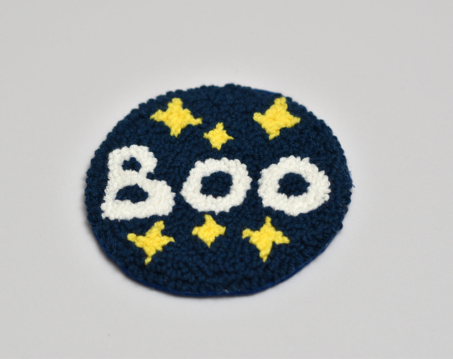 Embroidered coaster with 'BOO' text and yellow stars on a blue background