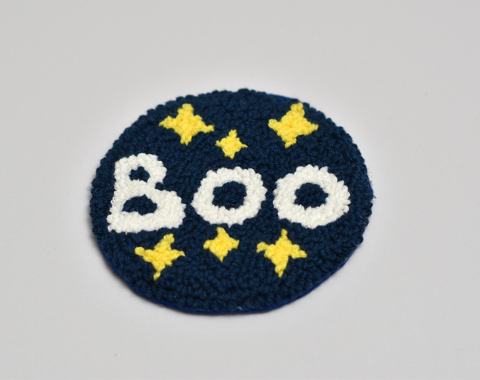 Embroidered coaster with 'BOO' text and yellow stars on a blue background