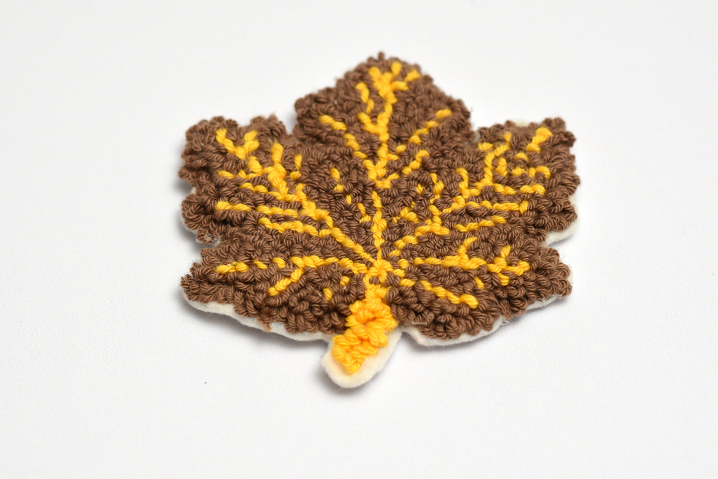 Punch needled  leaf-shaped coaster with brown and yellow colors on a white background