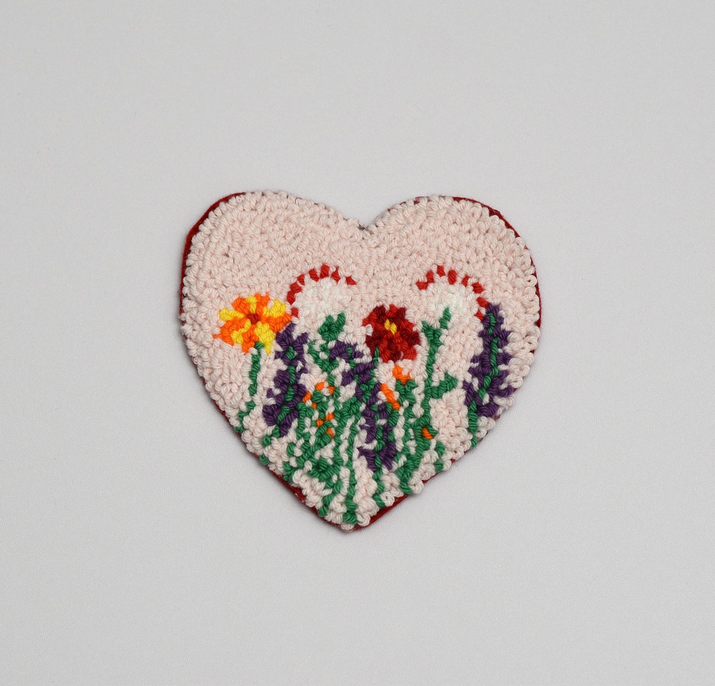 Heart-shaped embroidered coaster with floral design on a light gray background