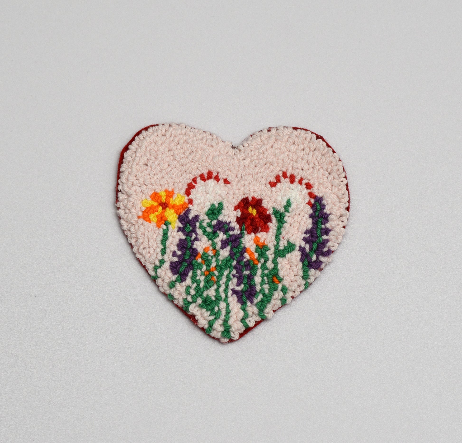 Heart-shaped embroidered coaster with floral design on a light gray background
