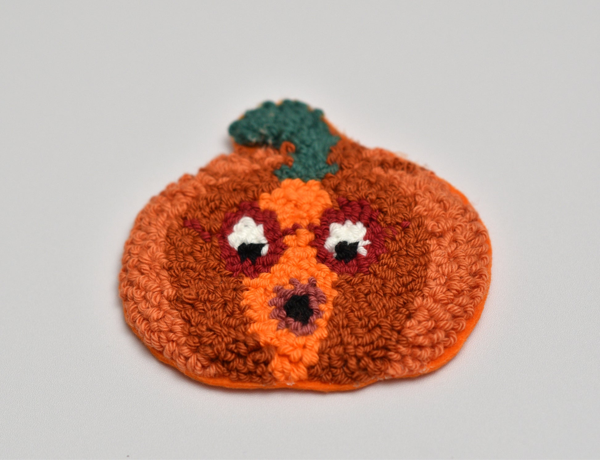 Punch needled pumpkin coaster with a face on a gray background