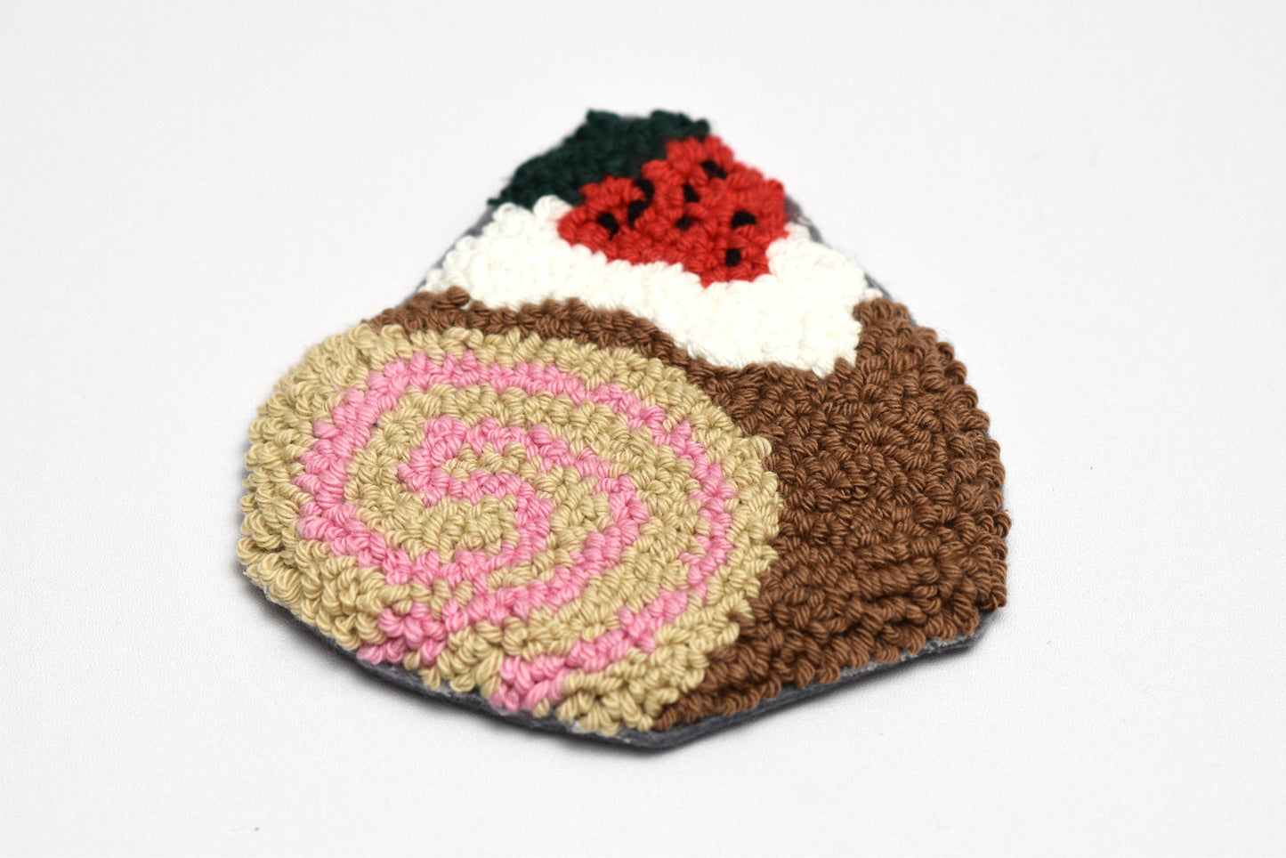 Embroidered cake-shaped rug with pink swirl and brown base on a white background