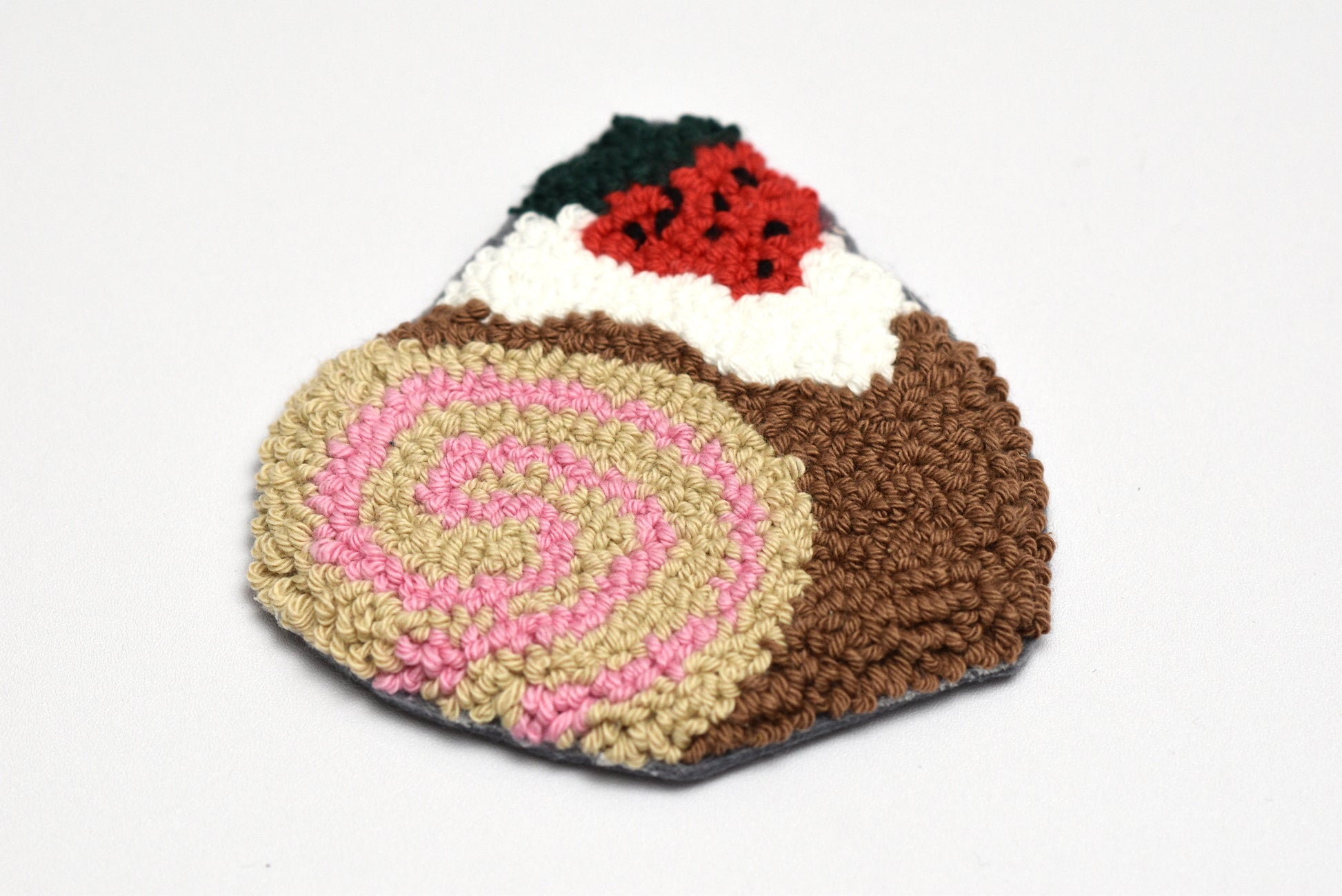 Embroidered cake-shaped rug with pink swirl and brown base on a white background