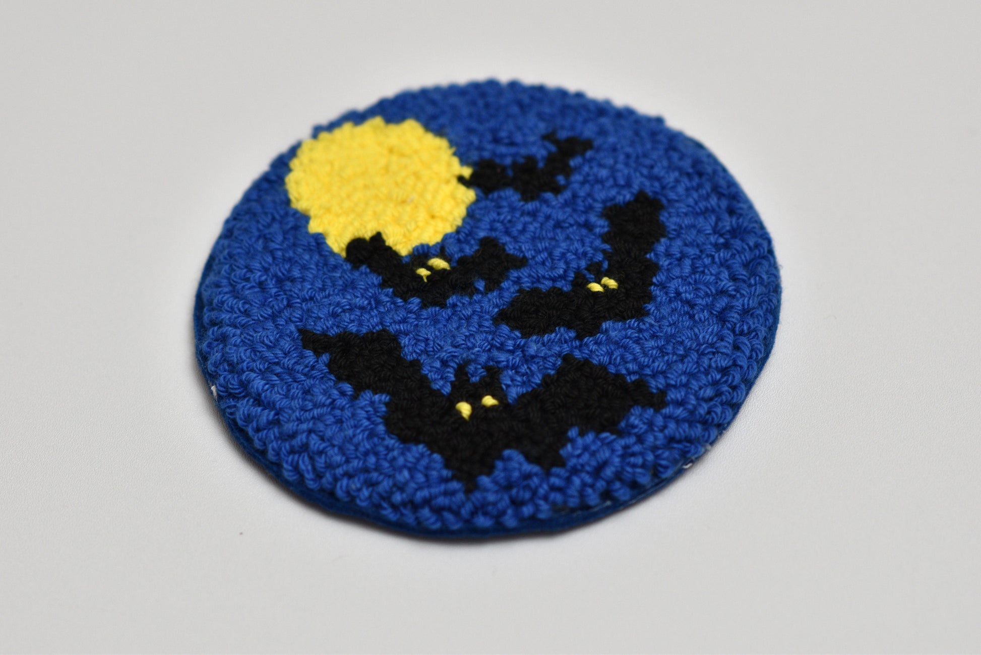 Round blue mug rug with black bats and a yellow moon on a gray background