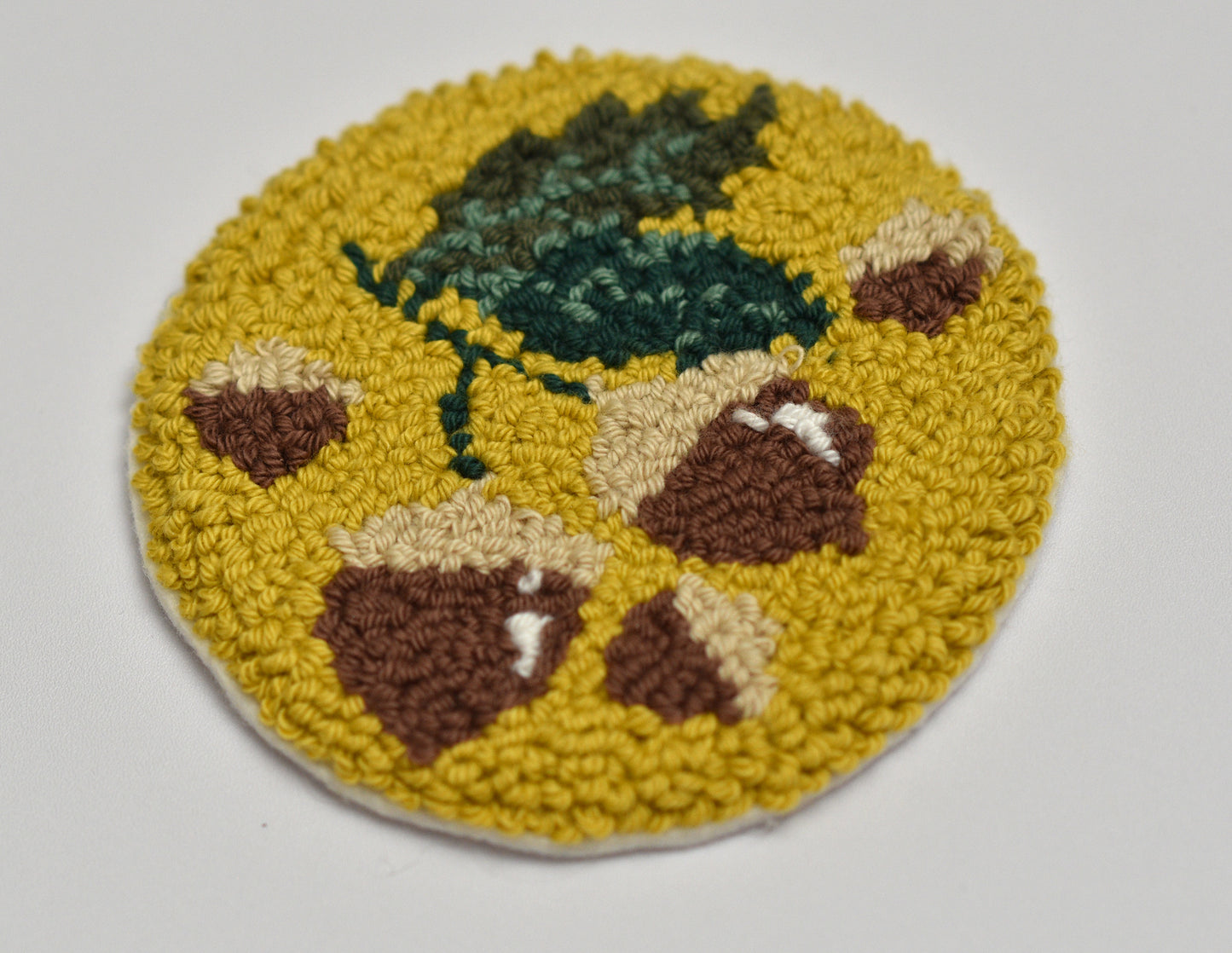 Round punch needle coaster with autumn design including hazelnut and leaves on a white background