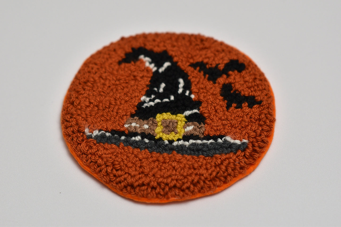 Punch needle coaster with a witch's hat design on an orange background