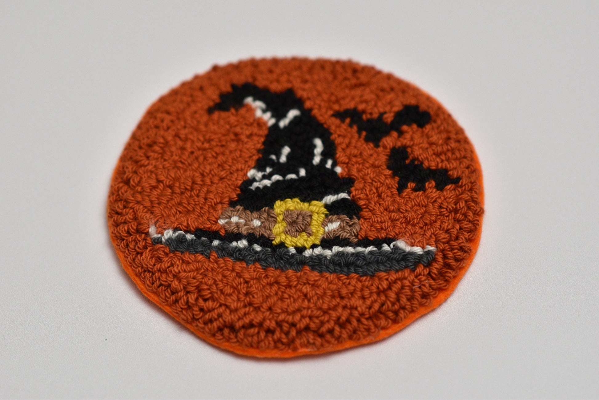 Punch needle coaster with a witch's hat design on an orange background