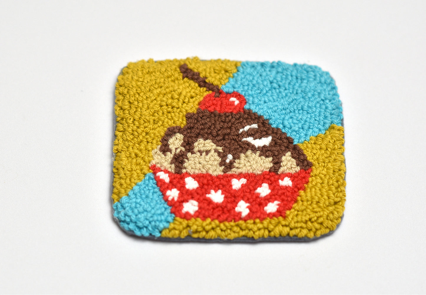Square woven punch needle coaster with a dessert design on a white background