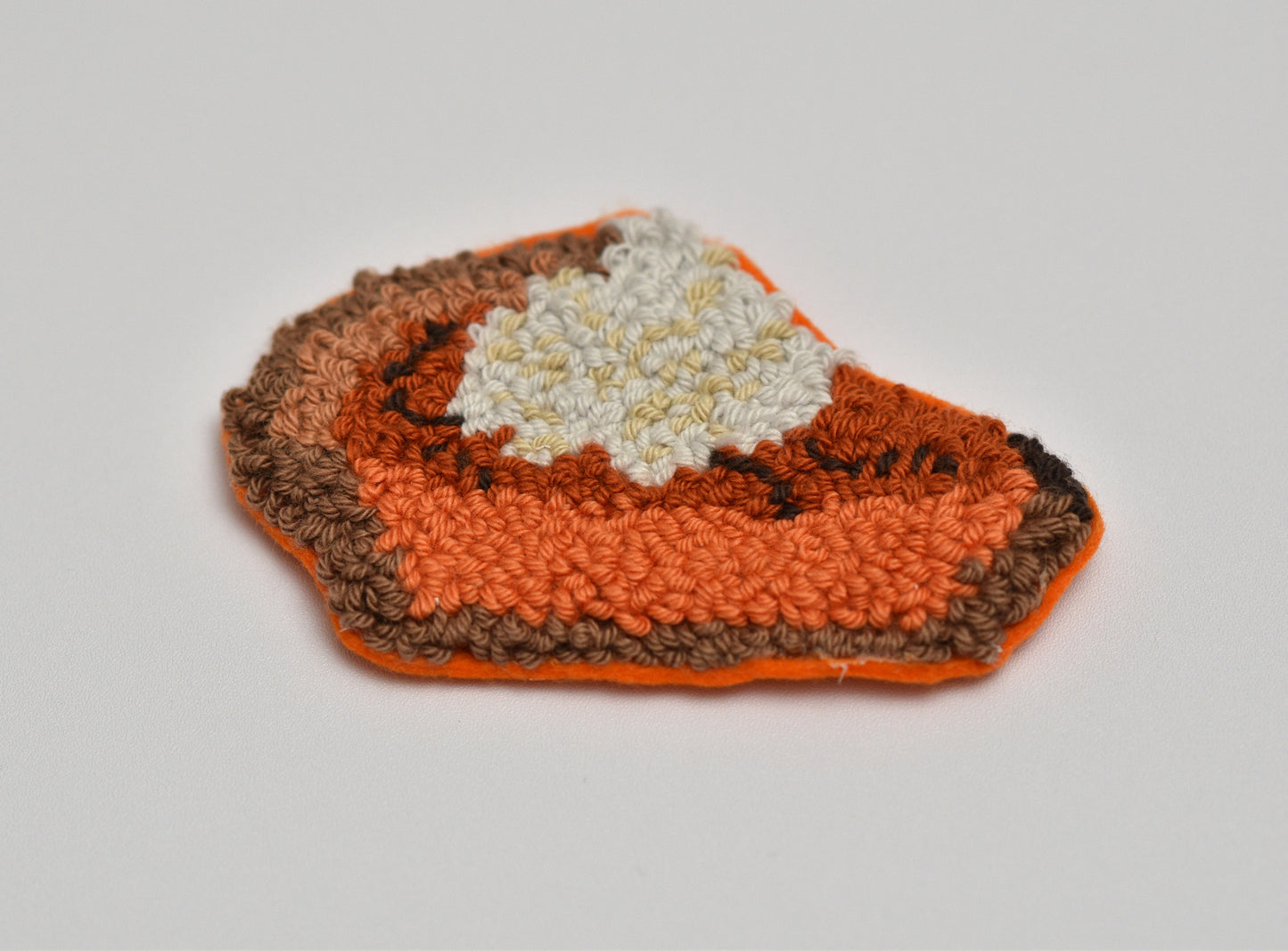 Punch needled coaster with pumpkin pie slice design on a light gray background
