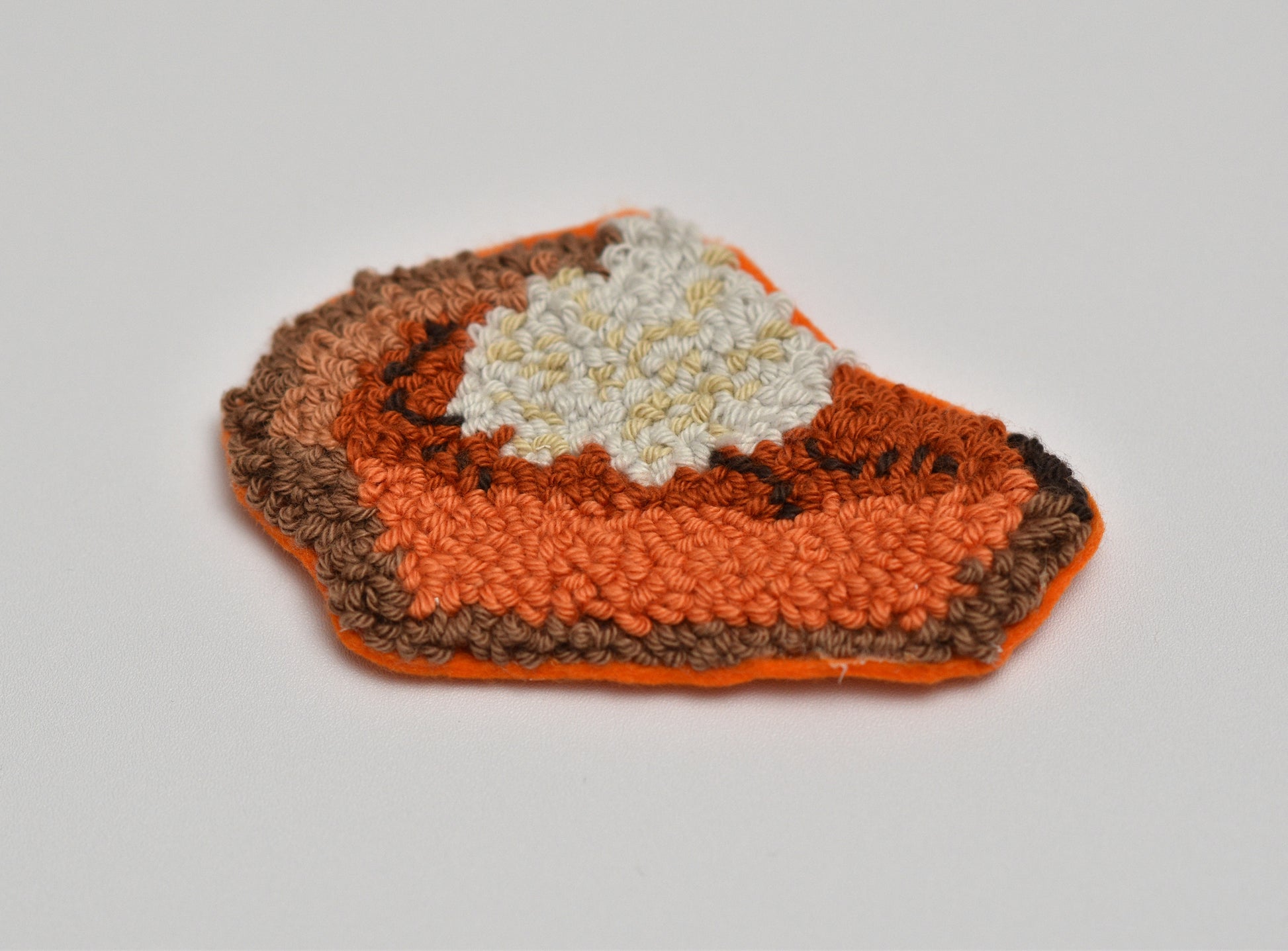 Punch needled coaster with pumpkin pie slice design on a light gray background
