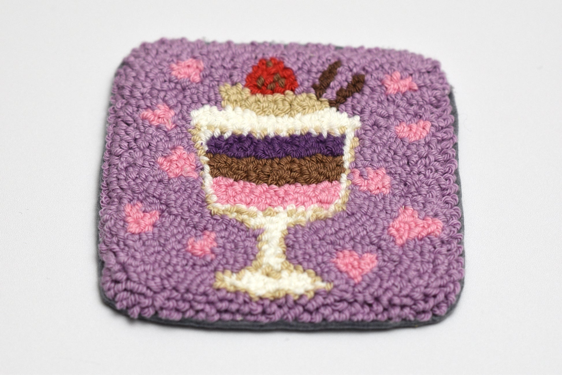 Square textured punch needle coaster with a parfait dessert design on a light gray background