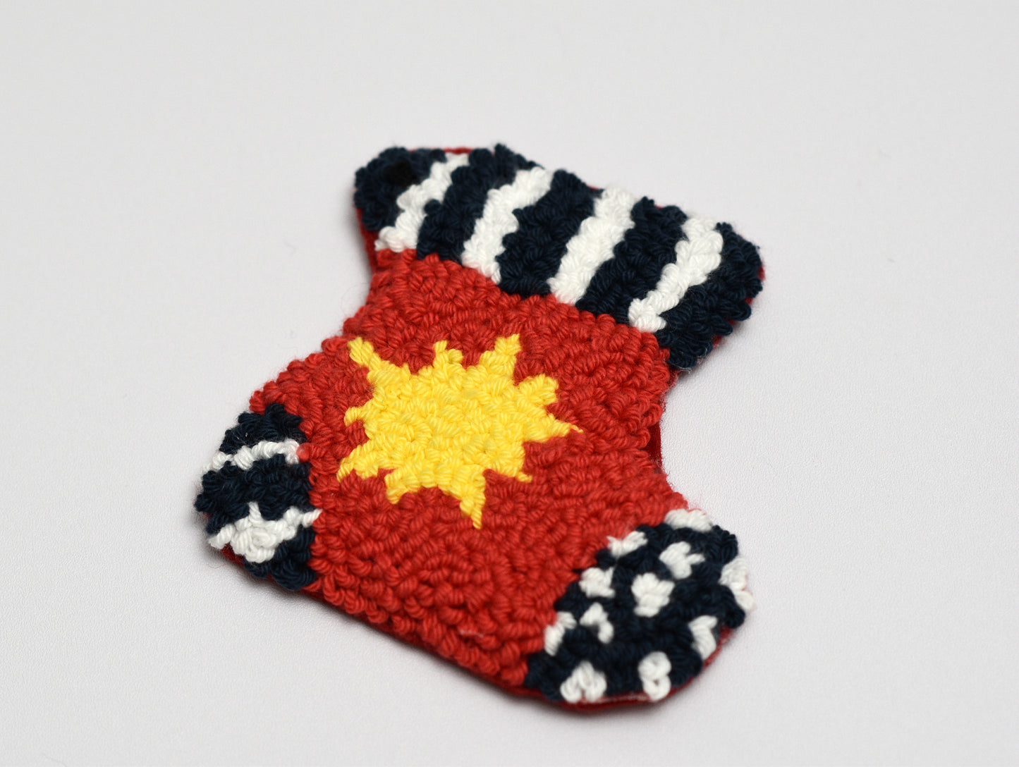 Christmas-Themed Punch needle coaster with a red background, yellow center, and black and white pattern on a light gray background