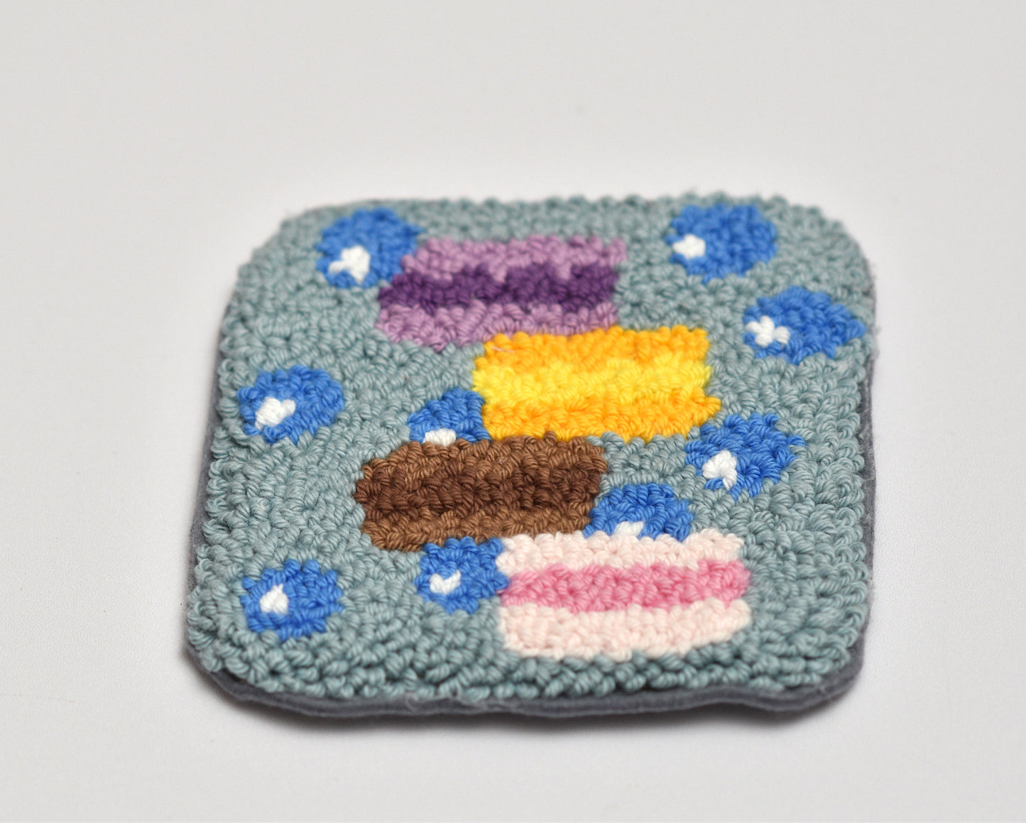 Square woven punch needle coaster with colorful macaron design on a light gray background