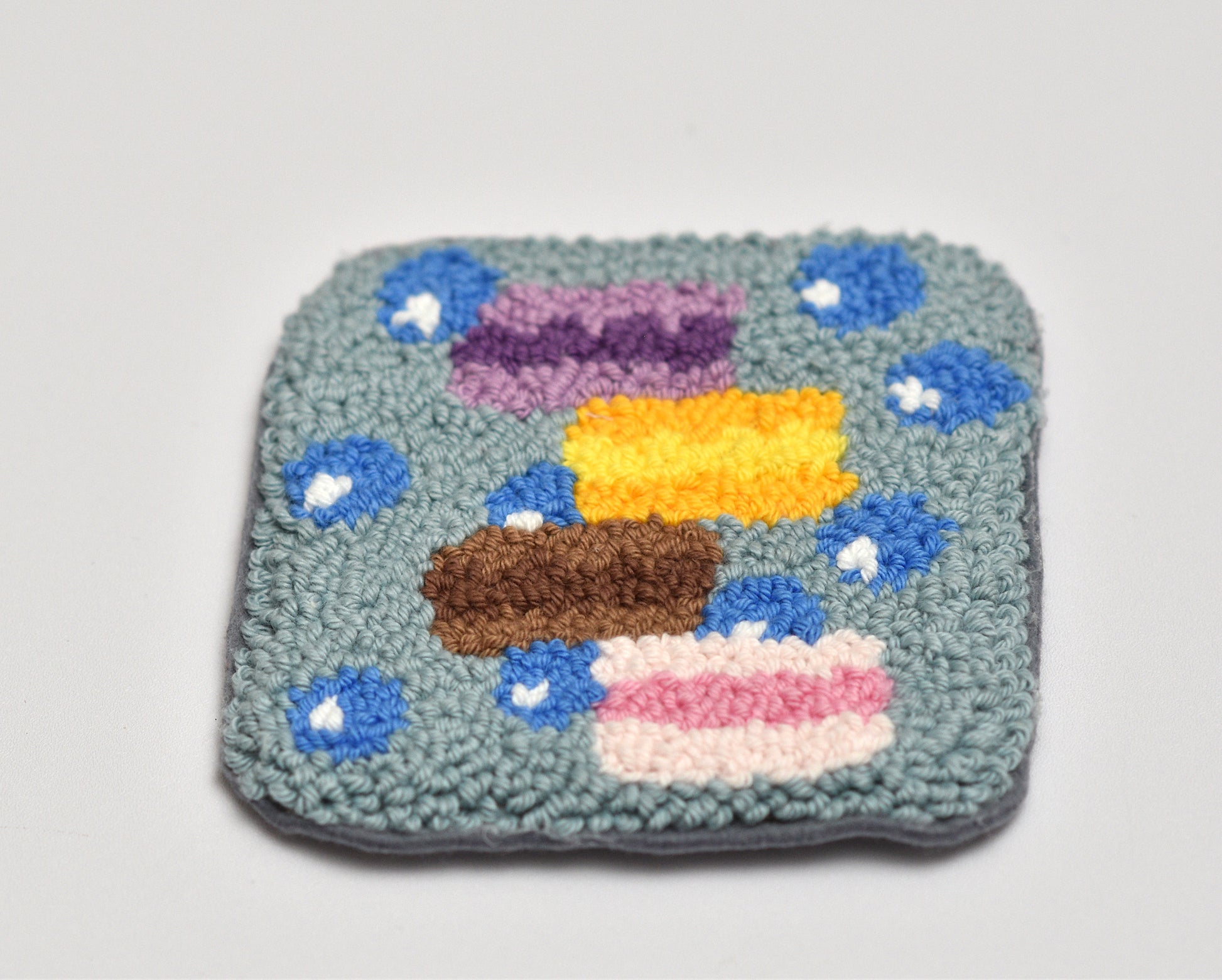Square woven punch needle coaster with colorful macaron design on a light gray background