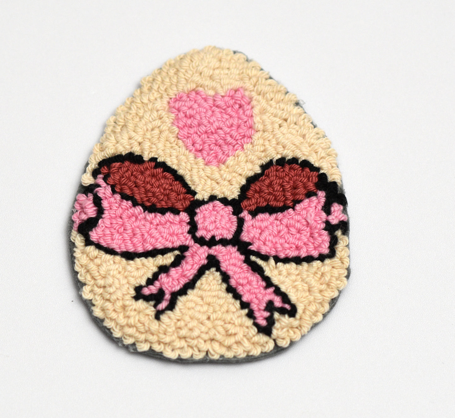Decorative Easter egg-shaped mug rug with a pink bow design on a light gray background