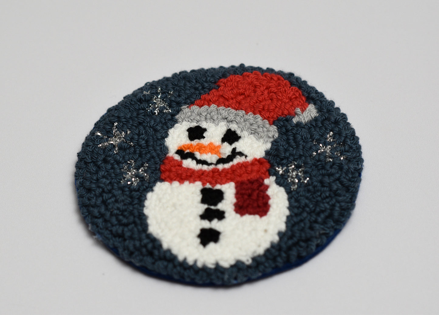 Round punch needled coaster with a snowman design on a gray background
