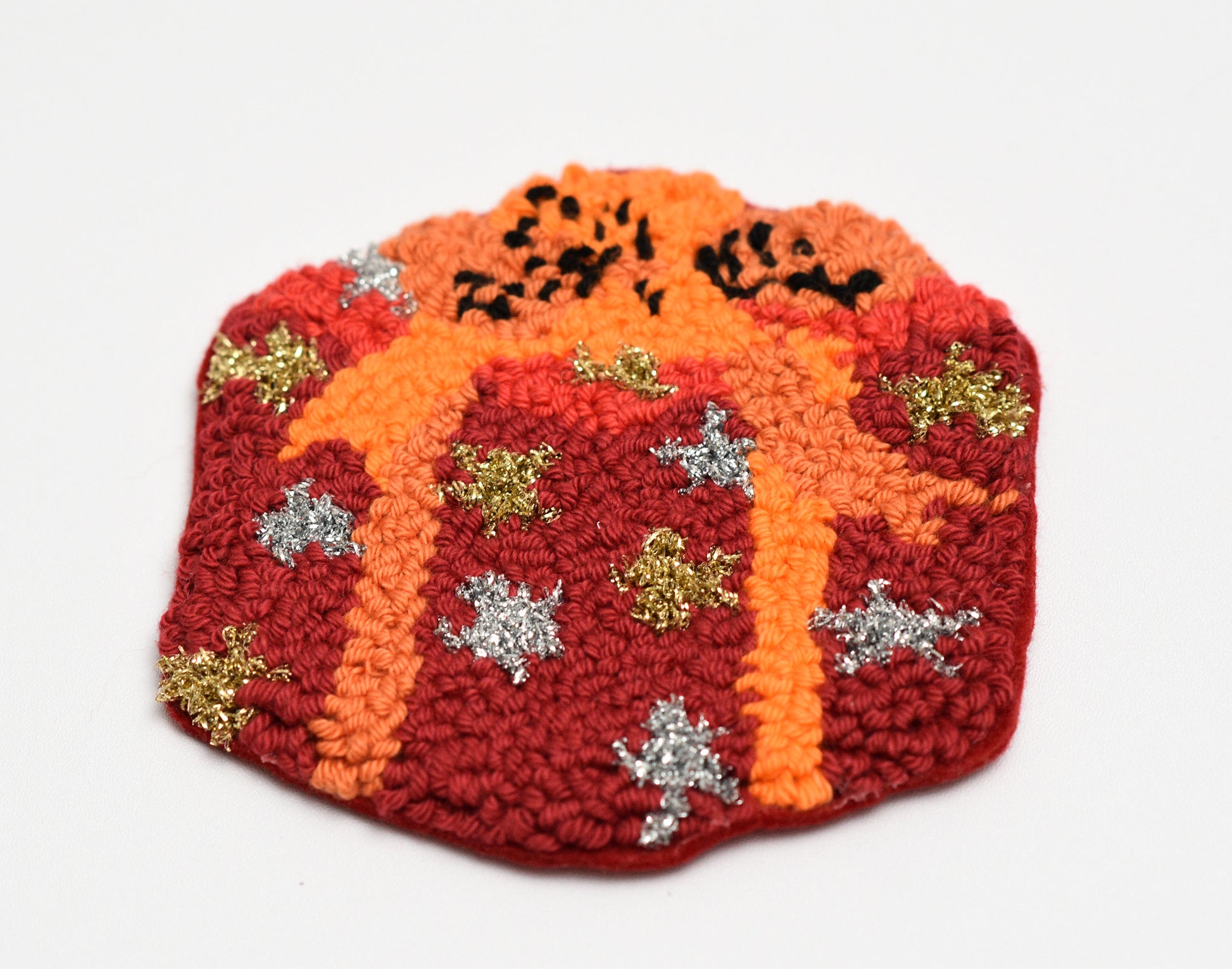 Decorative punch needled coaster with orange and red colors and decorative elements on a white background