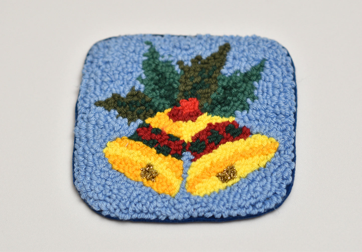 Decorative punch needled mug rug with Christmas yellow bells and green holly on a blue background