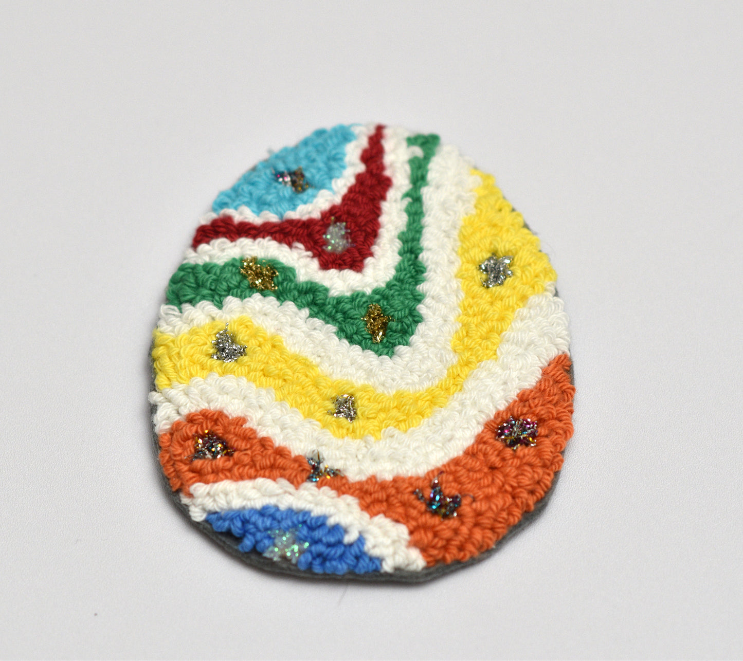 Colorful woven egg-shaped coaster with a pattern on a light gray background