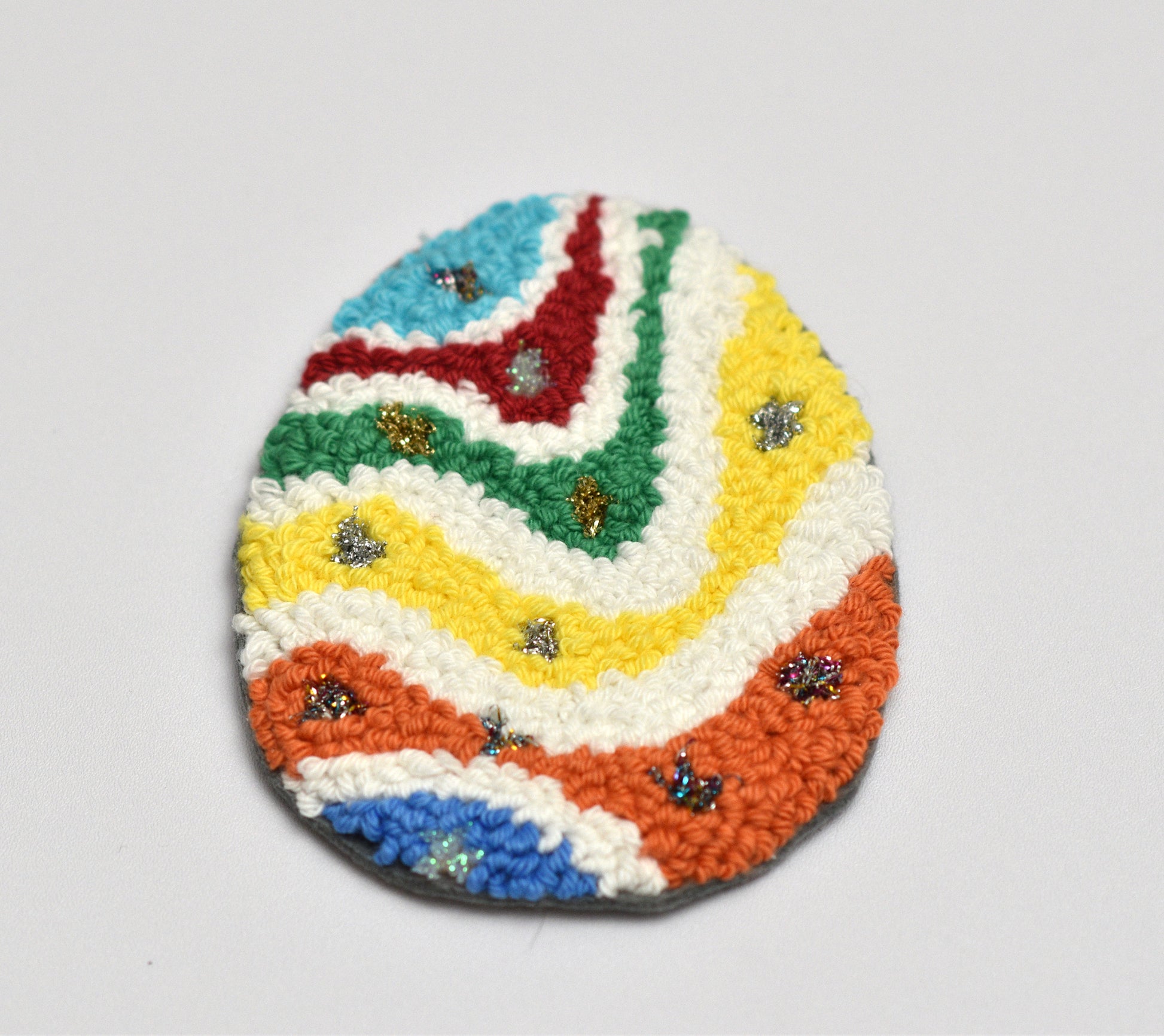 Colorful woven egg-shaped coaster with a pattern on a light gray background