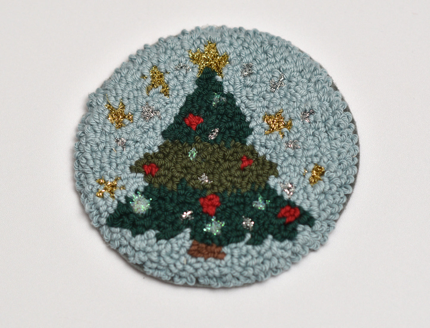 Round punch needled mug rug with a Christmas tree design on a light gray background