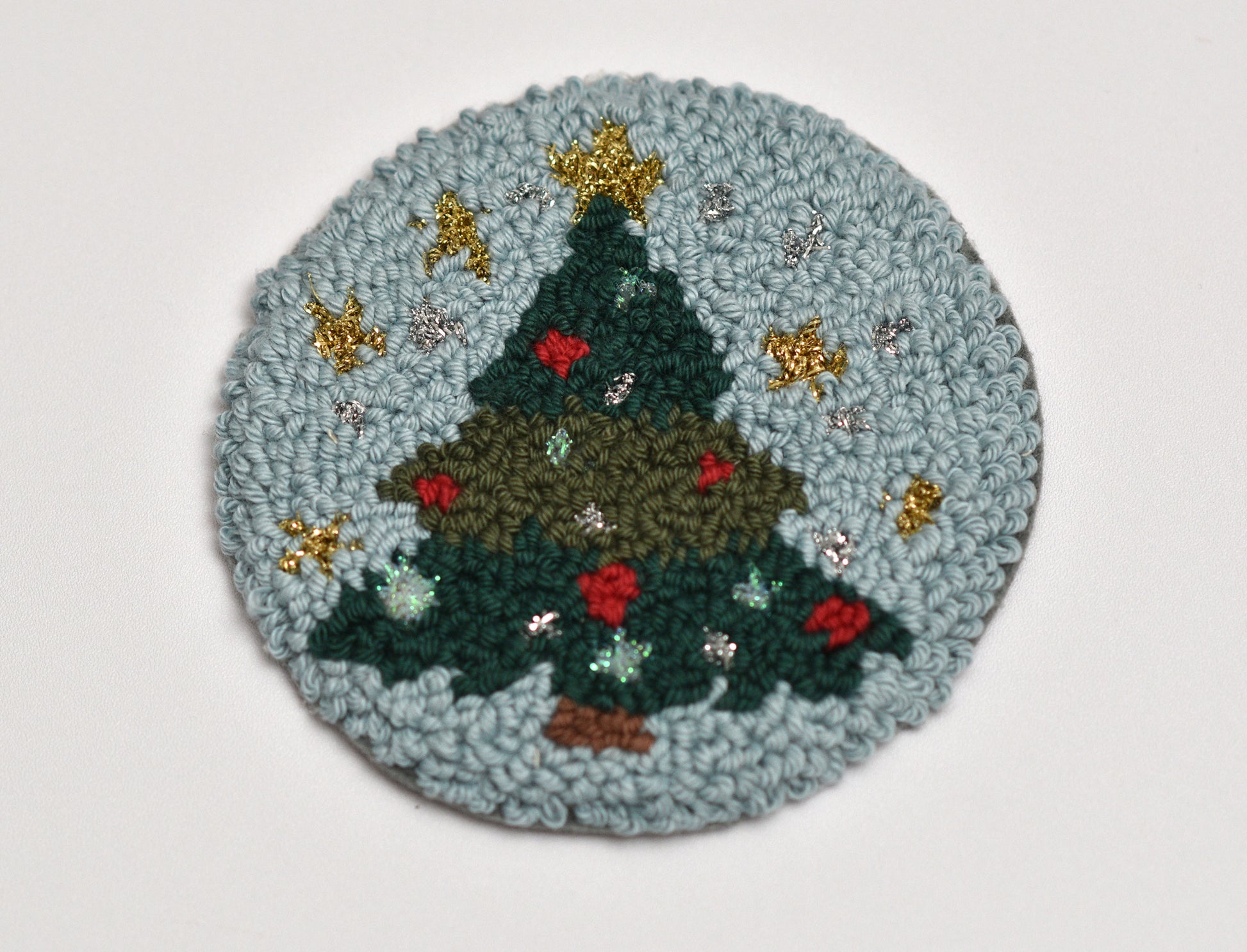 Round punch needled mug rug with a Christmas tree design on a light gray background