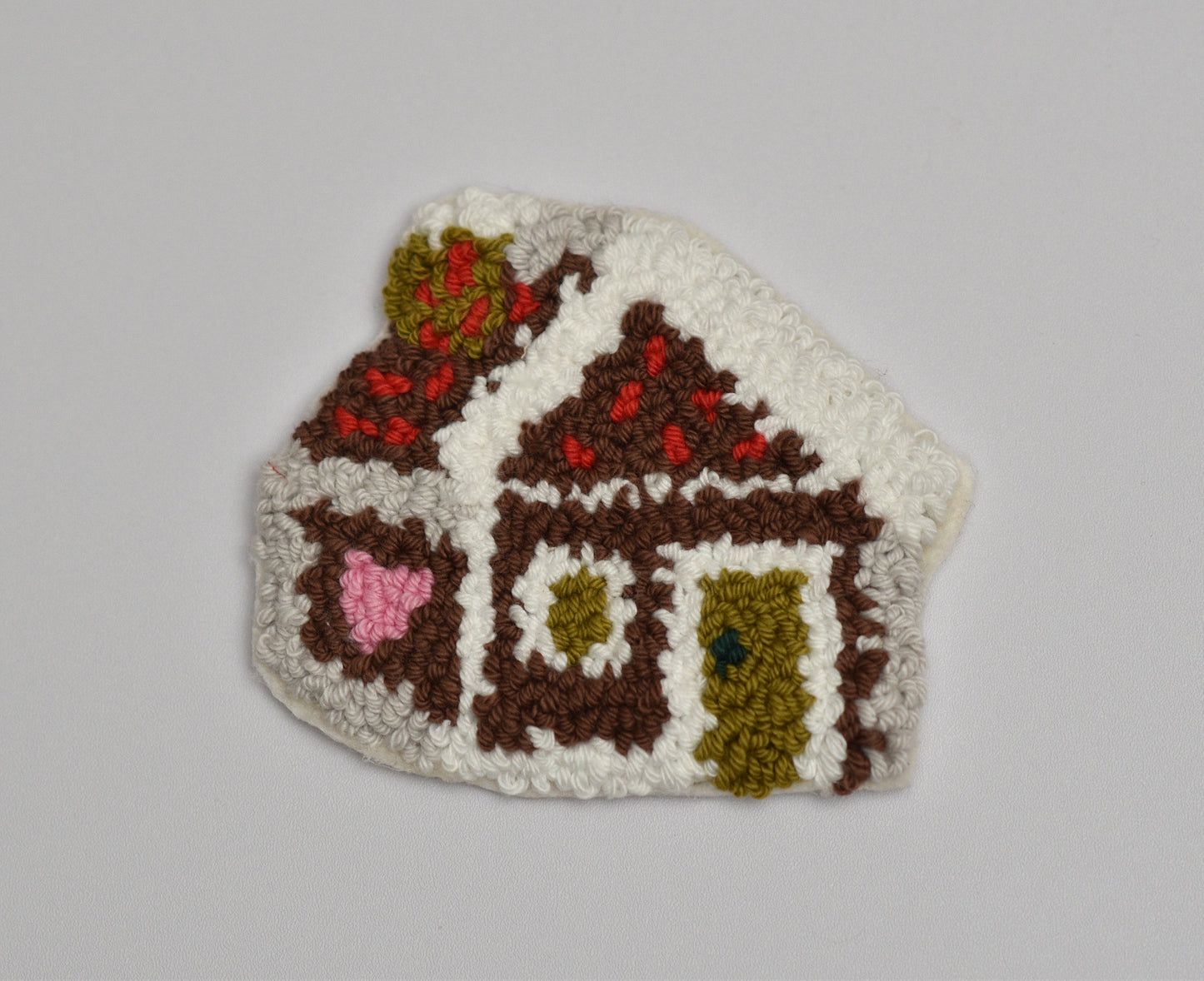 Punch needled coaster with gingerbread house design on a plain background