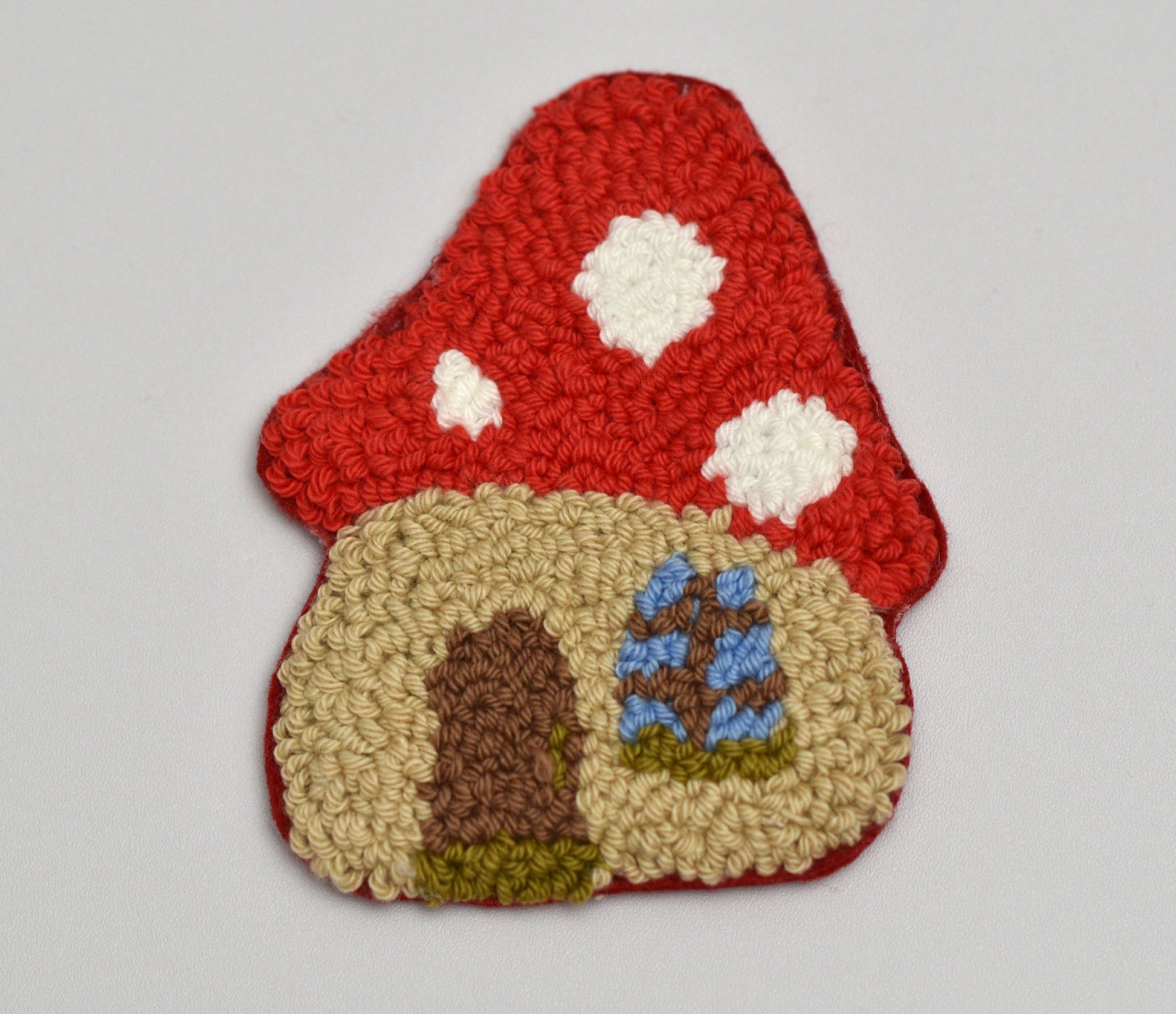 Punch needle coaster with mushroom with a door and windows on a gray background