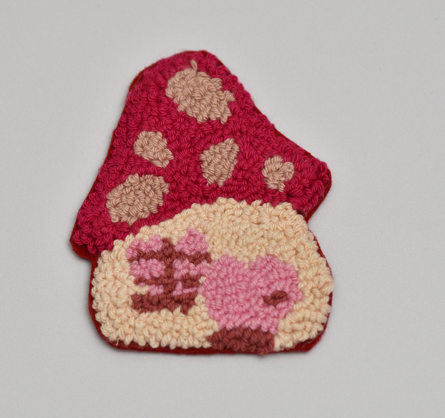 Punch needled coaster with pink and beige mushroom design on a gray background