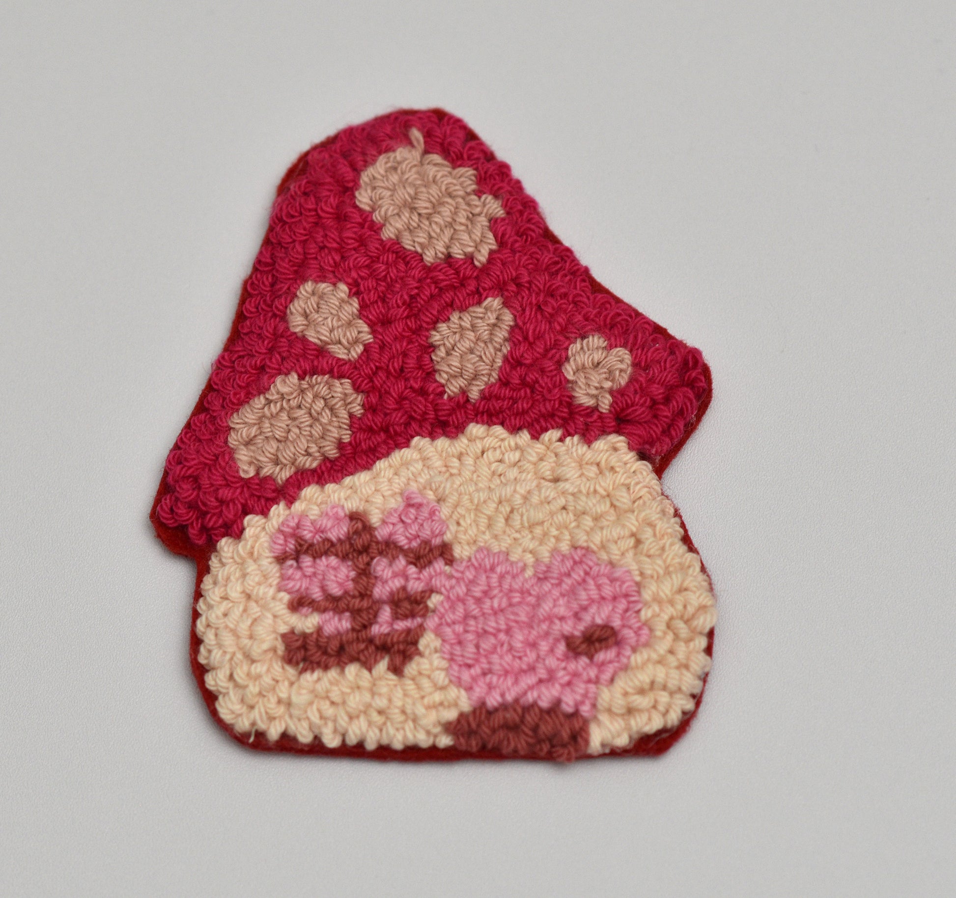 Punch needled coaster with pink and beige mushroom design on a gray background