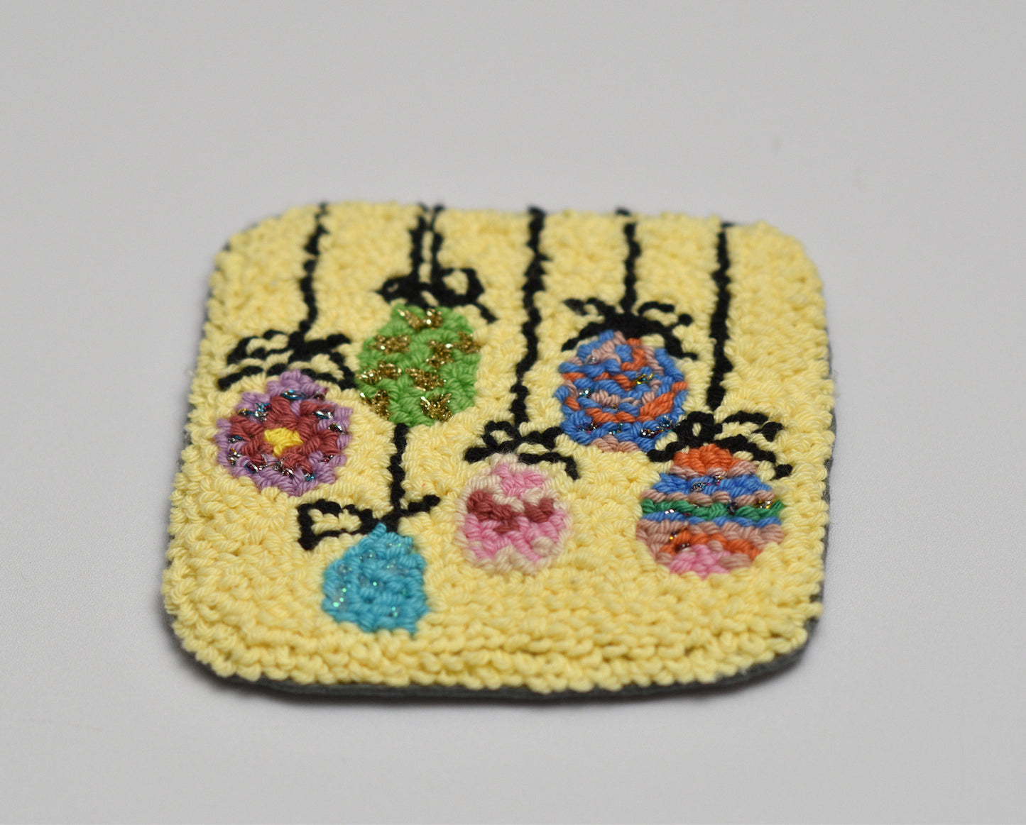 Square woven Easter Egg coaster with floral design on a gray background